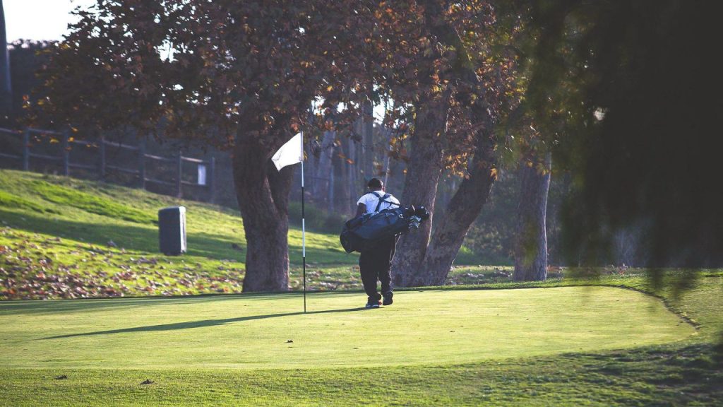 Golfer carrying equipment across a putting green at Lake Forest Golf and Practice Center during a quiet morning practice session